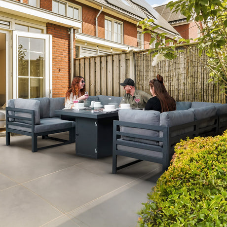 Stylish outdoor dining set with gray cushions, a black table, and three people enjoying a meal in a cozy garden setting
