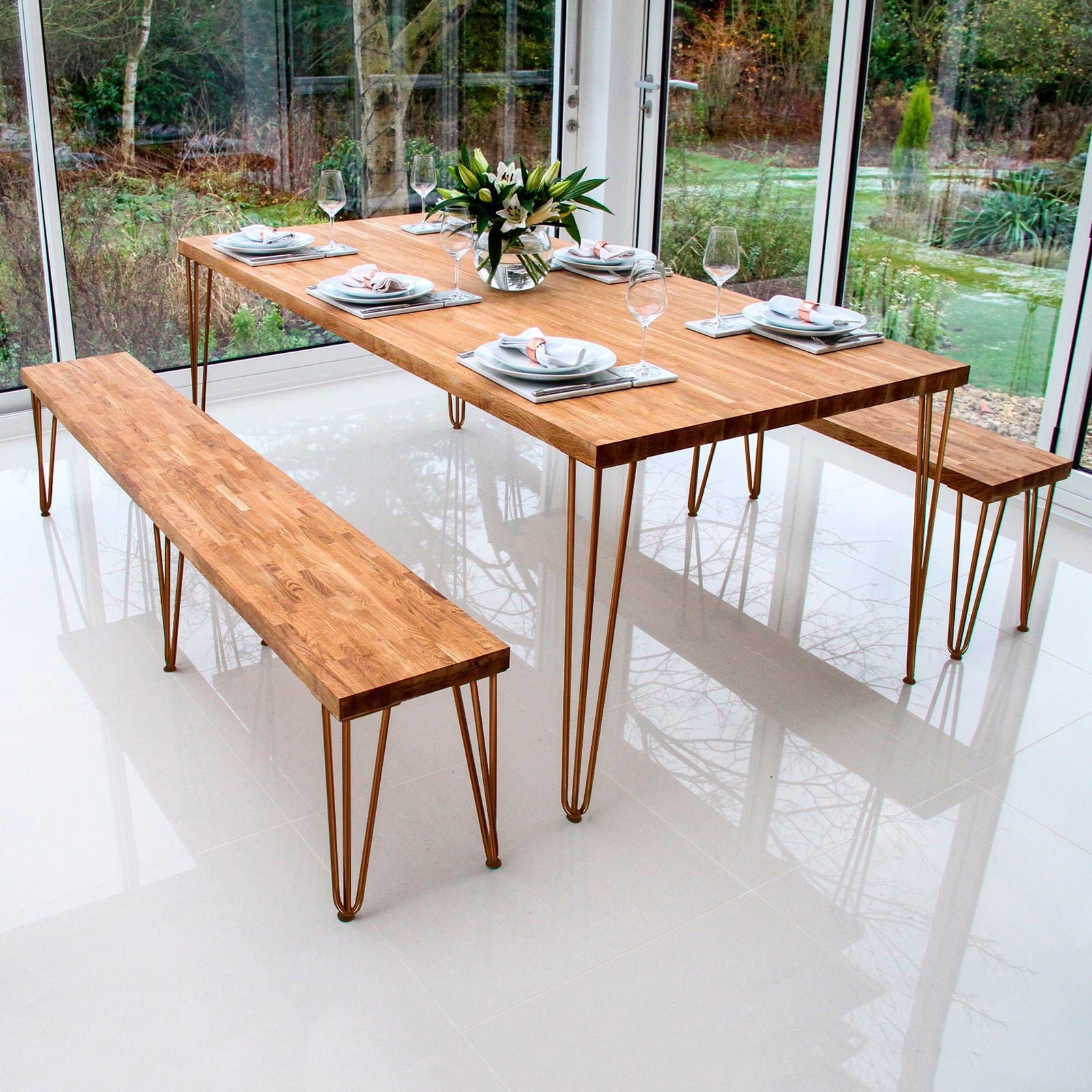 Stylish wooden dining table with metal legs, set with plates and glasses, surrounded by a bright, modern glass-walled room