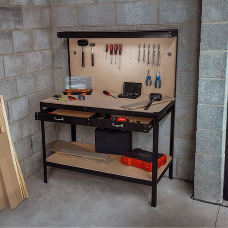 A sturdy black workbench with tools, including pliers, wrenches, and a hammer, set against a gray concrete wall in a workshop