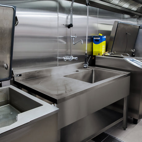 Stainless steel catering sink with a smooth surface, wall-mounted faucet, and adjacent equipment in a commercial kitchen setting