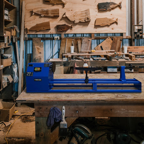 Blue woodworking lathe on a wooden workbench, surrounded by tools and wood pieces, in a rustic workshop setting